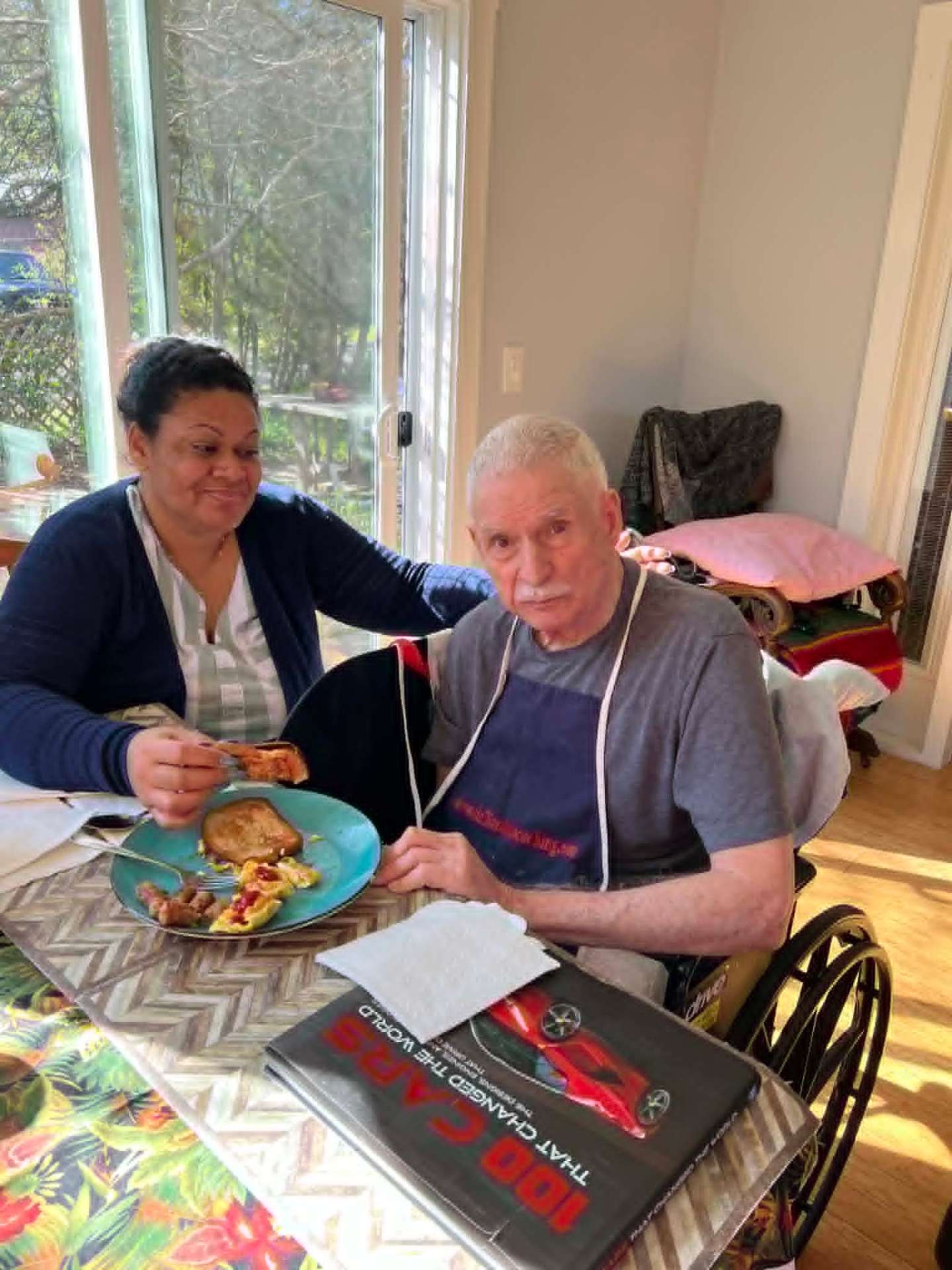 A caregiver sharing breakfast with an elderly gentleman by a sunlit window